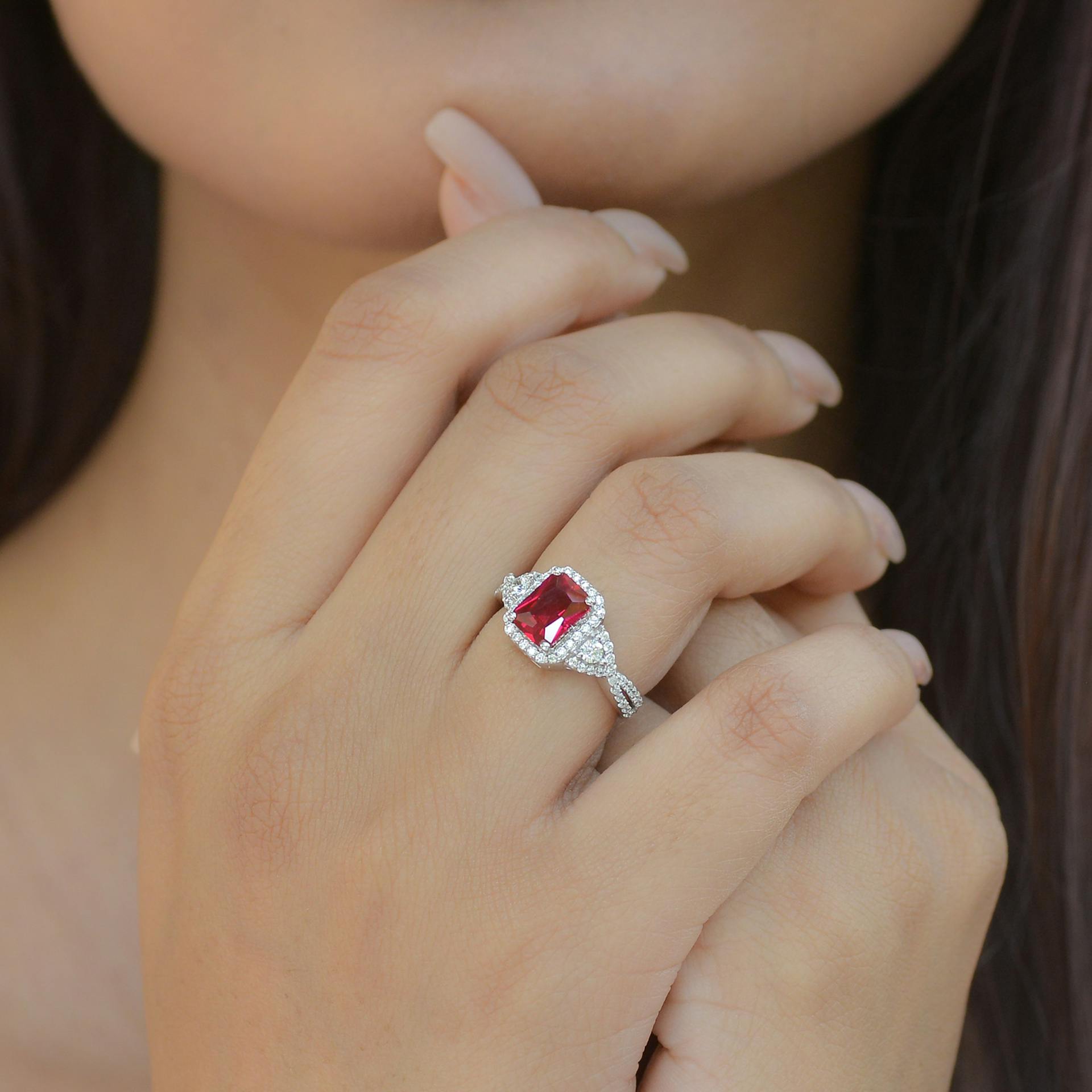 Close-up of a hand wearing a ring with a deep red rectangular gemstone surrounded by small diamonds on a silver band.
