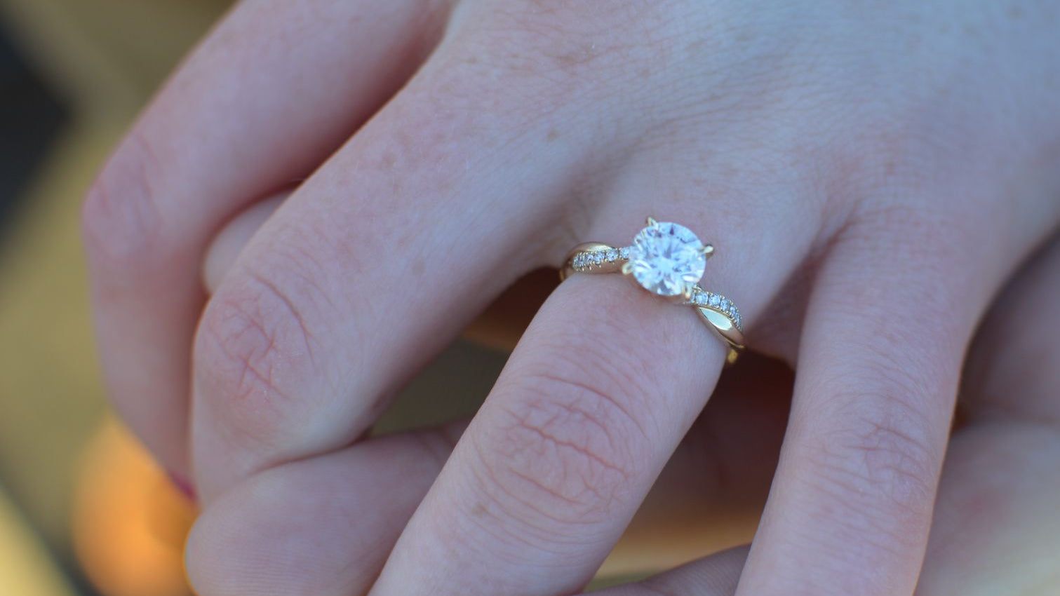 Close-up of a hand wearing a diamond ring with a blurred background